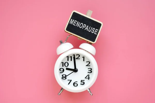 Reloj despertador y palabra menopausia sobre fondo rosa . — Foto de Stock