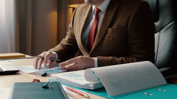 Egy öltönyös üzletember üzleti táblázatokkal és pénzügyi jelentésekkel dolgozik. Dokumentumokkal való munka az irodában. — Stock videók
