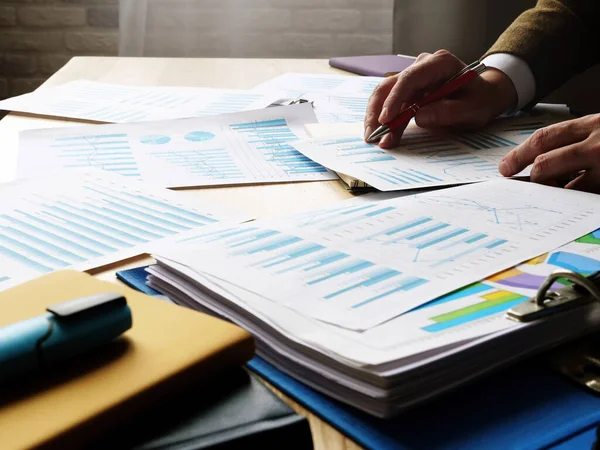 Ein Stapel Papiere mit Daten und Diagrammen auf dem Tisch. Ein Mann prüft die Jahresabschlüsse. — Stockfoto