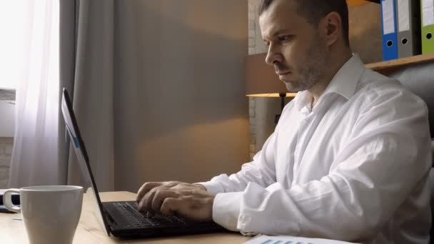 Ofisinde dizüstü bilgisayarla çalışan odaklanmış bir iş adamı. Bir adam masaya oturur ve klavyeye yazar.. — Stok video