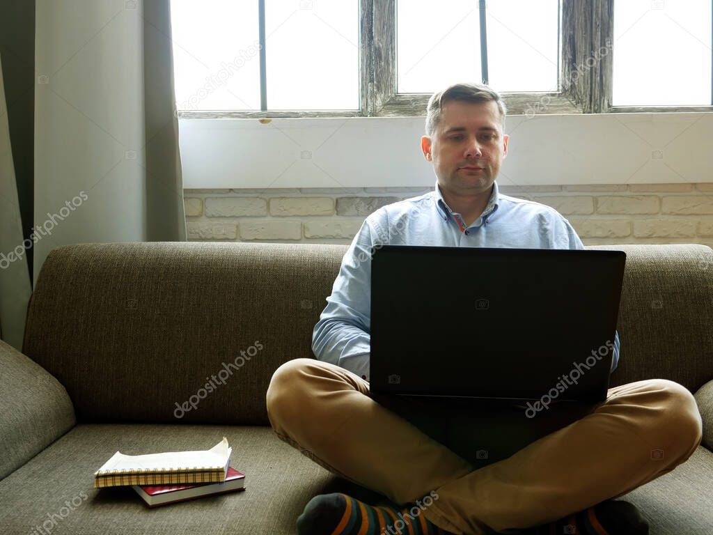 Man with laptop works at home. Quarantine concept. Freelancer sits on the couch and types on the keyboard.