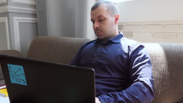 Freelancer sentado em um sofá trabalhando em um laptop . — Vídeo de Stock