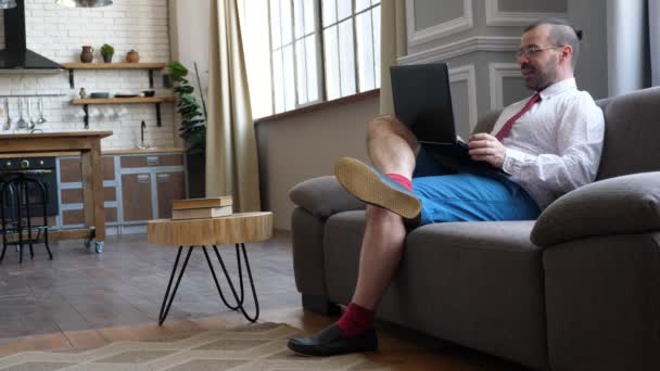 Trabalha em casa em quarentena. Empresário no sofá conversando em vídeo chat. Um homem de calções e gravata . — Vídeo de Stock