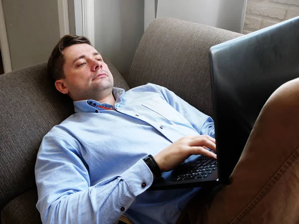 Trabajo remoto. Un hombre en casa en el sofá trabaja con un portátil . — Foto de Stock