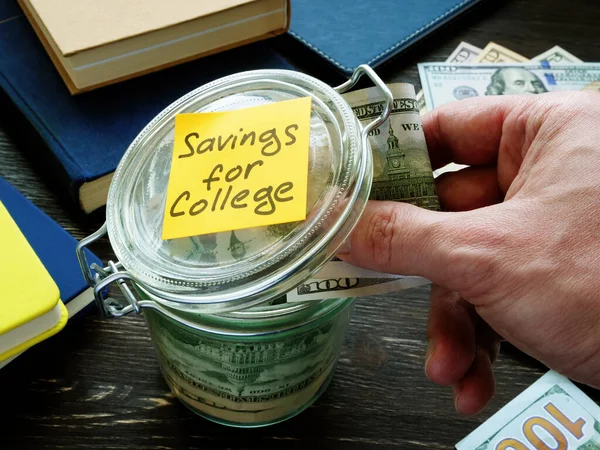Сбережения для колледжа. Рука кладет деньги в стеклянную банку . — стоковое фото