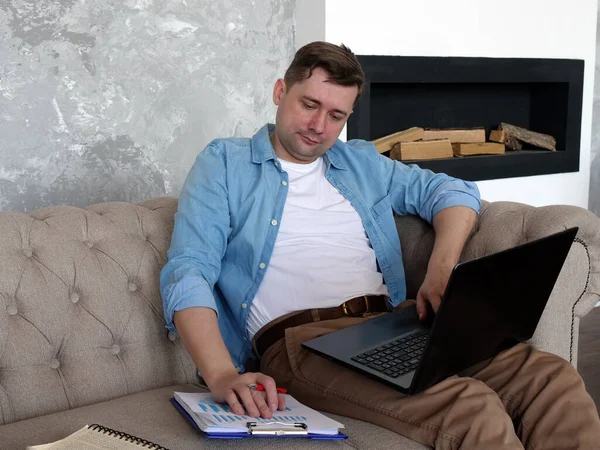 Concepto de cuarentena. El tipo en casa en el sofá revisa el informe financiero . — Foto de Stock