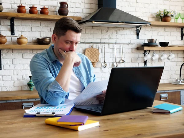 El joven trabaja remotamente con documentos financieros. Trabajo desde casa. — Foto de Stock