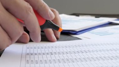 Finansal raporda işaretli rakamların altını çizen ellerin yakın plan görüntüsü.