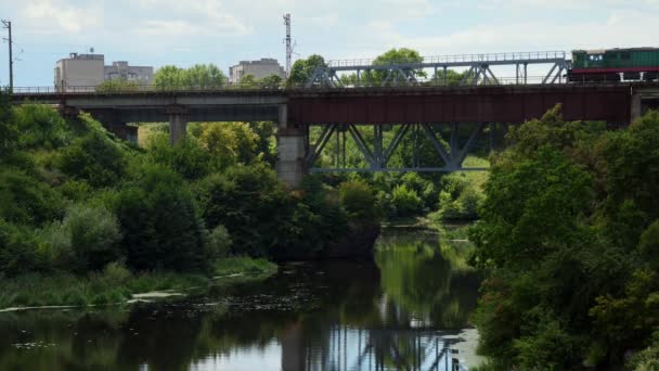 Un wagon couvert traverse lentement un pont métallique en été. — Video