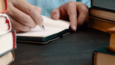 Kütüphanede elinde kitap olan bir adam not defterine not alır. Öğrenme kavramı.