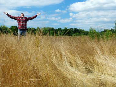 Neşeli genç adam doğada bir tarlada dururken ellerini gökyüzüne uzatıyor. Neşe ve rahatlama.