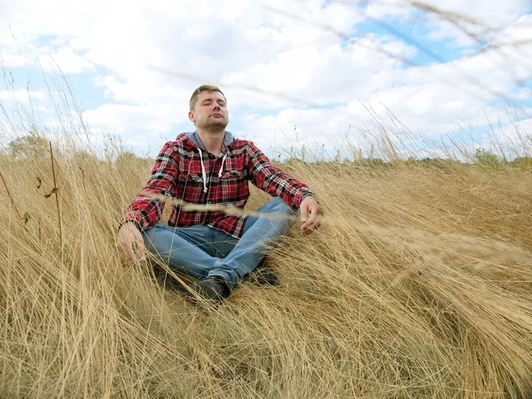 Молодой турист сидит в траве на осеннем поле. Расслабление и медитация. — стоковое фото