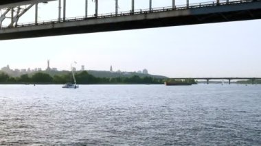 Yazın Kyiv ve Dnipro manzarası. Bir yat ve bir mavna nehir kıyısındaki köprüde yüzüyor..