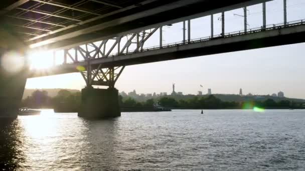 Ein Boot und ein Lastkahn fahren unter einer Brücke über den sommerlichen Dnjepr in Kiew, Ukraine. — Stockvideo