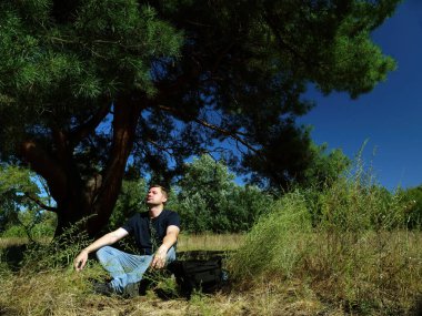 Erkek turist ormanda bir ağacın altında otururken meditasyon yapar..