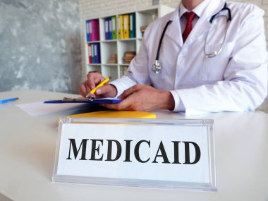 Üzerinde yazı olan bir plaka ve belgeleri dolduran bir doktor..
