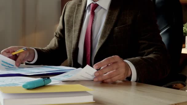 Un uomo d'affari in giacca e cravatta si siede a un tavolo e lavora con le relazioni finanziarie. Documenti ravvicinati. — Video Stock