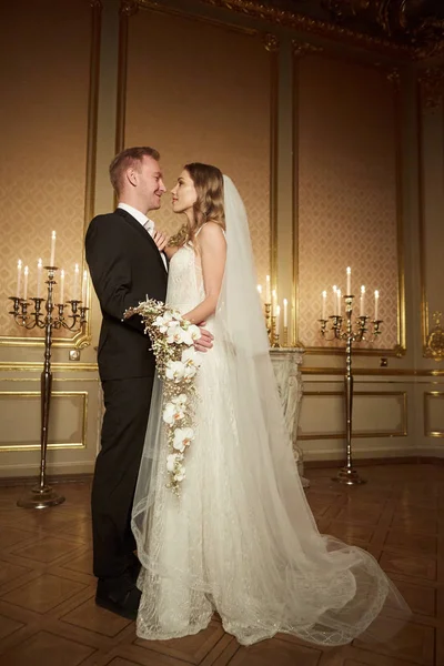 Couple de mariage dans un intérieur luxueux dans le style baroque se serre dans ses bras. Belle fille modèle en robe blanche. Un homme en costume. Mariée beauté avec marié. Portrait féminin et masculin. Femme avec dentelle — Photo