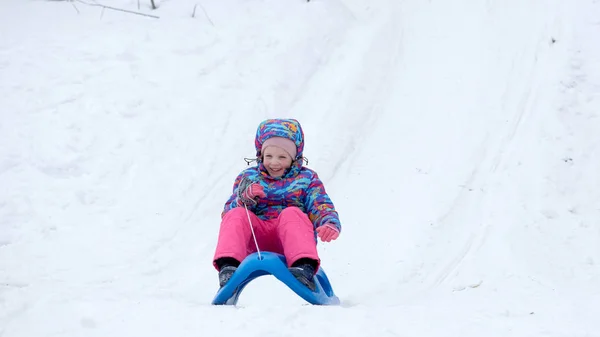 白い晴れた冬の山の風景の中で雪に覆われたそりの歩道でそりに乗る陽気な女の子 — ストック写真