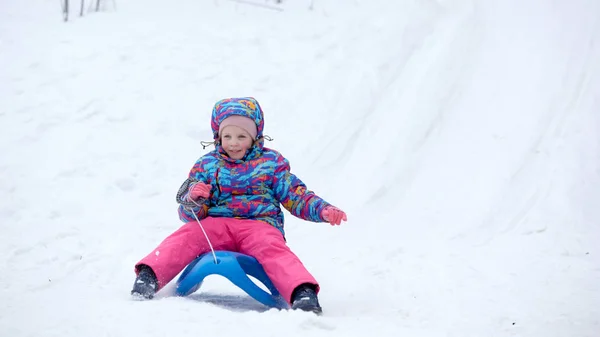 Fröhliches Mädchen beim Schlittenfahren auf einer schneebedeckten Rodelbahn in einer weißen, sonnigen Winterberglandschaft — Stockfoto