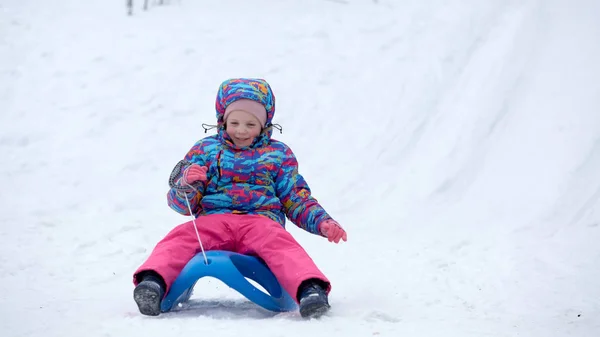 白い晴れた冬の山の風景の中で雪に覆われたそりの歩道でそりに乗る陽気な女の子 — ストック写真