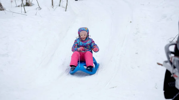 Vrolijk meisje rijden een slee bergafwaarts op een besneeuwde slee parcours in een witte zonnige winter berglandschap — Stockfoto