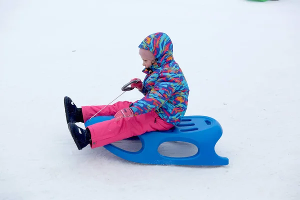 白い晴れた冬の山の風景の中で雪に覆われたそりの歩道でそりに乗る陽気な女の子 — ストック写真
