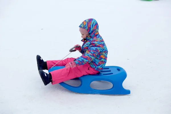 Fröhliches Mädchen beim Schlittenfahren auf einer schneebedeckten Rodelbahn in einer weißen, sonnigen Winterberglandschaft — Stockfoto