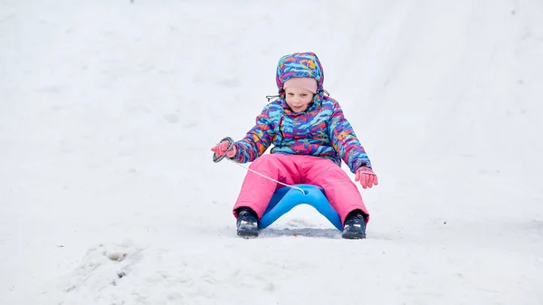 在雪地覆盖的雪橇小径上 一个快乐的女孩骑着雪橇下山 在一个阳光明媚的冬季山景中 — 图库照片