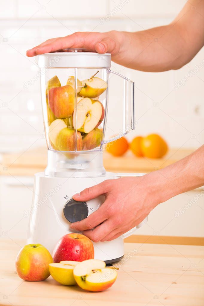 Young man cooking apple smoothie in blender