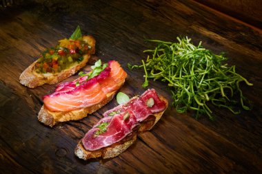 Kızarmış et, sebze ve Yeşiller ile hafifçe tuzlanmış somon ile çeşitli bruschetta ahşap arka plan üzerinde bırakır.