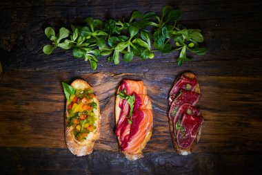 Kızarmış et, sebze ve Yeşiller ile hafifçe tuzlanmış somon ile çeşitli bruschetta ahşap arka plan üzerinde bırakır.