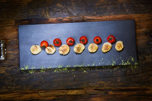 Gebratene Jakobsmuscheln mit Tomaten auf einem schwarzen Teller. flacher dof. — Stockfoto