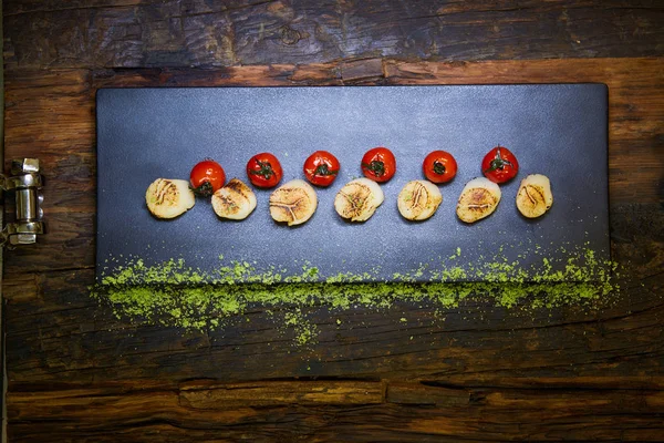 Жареные гребешки с помидорами на черной тарелке. Shallow dof . — стоковое фото