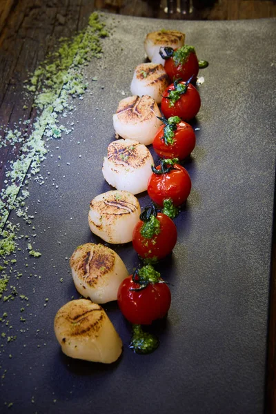 Gebratene Jakobsmuscheln mit Tomaten auf einem schwarzen Teller. flacher dof. — Stockfoto