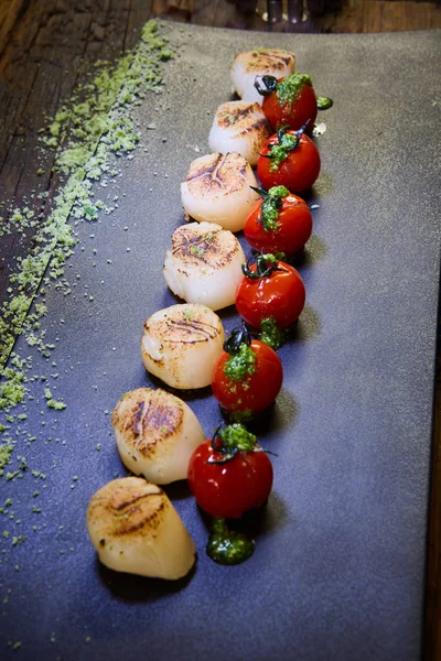 Жареные гребешки с помидорами на черной тарелке. Shallow dof . — стоковое фото