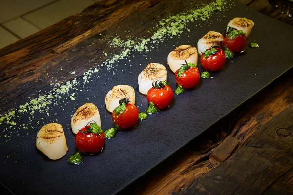 Gebakken coquilles met tomaten op een zwarte plaat. Ondiepe dof. — Stockfoto