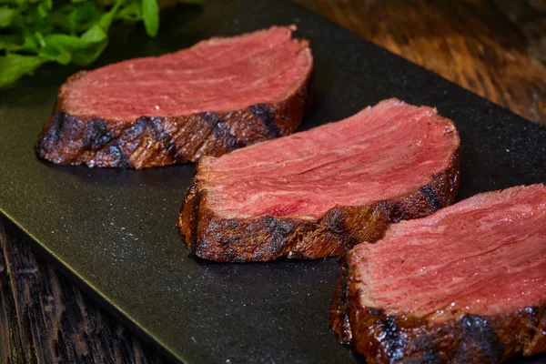 Стейк, разрезанный на куски, приготовленный, чтобы съесть говядину на каменном столе. — стоковое фото