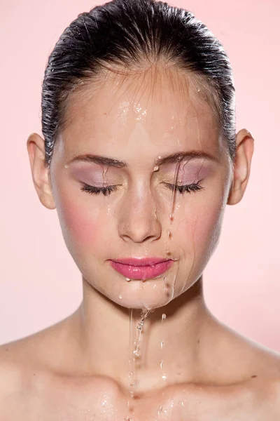 Mooi Model meisje met spatten van water op haar gezicht. Mooie vrouw onder plons water met frisse huid op roze achtergrond. Velletje zorgvuldigheid reiniging en hidratatie concept. Schoonheid gezicht — Stockfoto