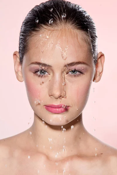 Belle fille modèle avec des éclaboussures d'eau sur son visage. Belle femme sous une goutte d'eau avec une peau fraîche sur fond rose. Soin de la peau Concept nettoyant et hydratant. Beauté visage — Photo