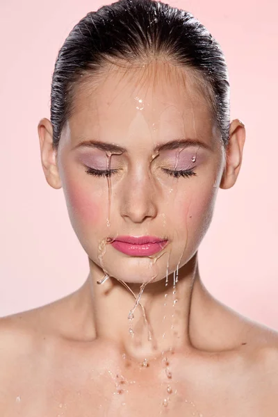 Belle fille modèle avec des éclaboussures d'eau sur son visage. Belle femme sous une goutte d'eau avec une peau fraîche sur fond rose. Soin de la peau Concept nettoyant et hydratant. Beauté visage — Photo