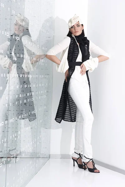 Hermosa mujer joven en sombrero blanco, tacones altos y traje blanco está de pie, mirando en la cámara. Estudio de larga duración sobre fondo blanco . — Foto de Stock