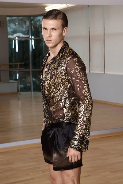 Man in elegant suite posing in fitness gym. High fashion young sexy man in shorts and a shirt decorated with gold.