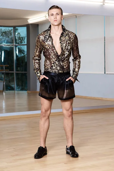 Man in elegant suite posing in fitness gym. High fashion young sexy man in shorts and a shirt decorated with gold.