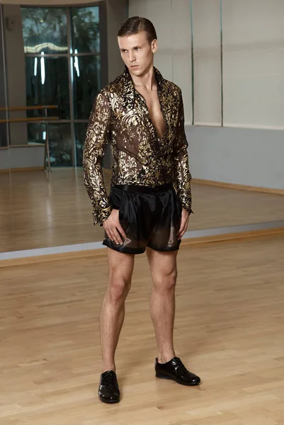 Man in elegant suite posing in fitness gym. High fashion young sexy man in shorts and a shirt decorated with gold.