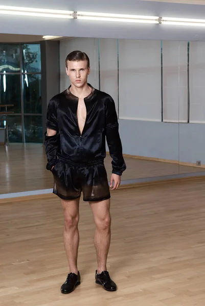 Man in elegant suite posing in fitness gym. High fashion young sexy man in black shorts and a black jacket