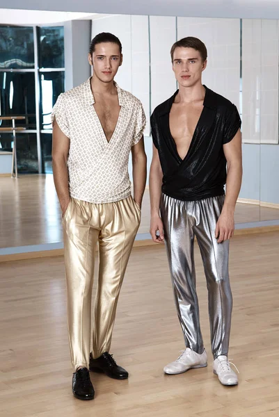 Deux hommes en costumes de sport élégants posant dans une salle de fitness. Jeunes hommes en legging sport argent et or — Photo