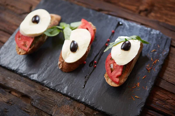 Bruschetta italiana con pomodoro tritato, basilico, mozzarella e aceto balsamico. Bruschetta caprese fresca fatta in casa o crostini su fondo in pietra nera, spazio copia . — Foto Stock