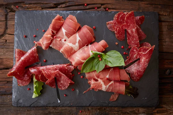 Tranches de crudo ou jamon de prosciutto italien aux feuilles de basilic frais sur fond noir . — Photo