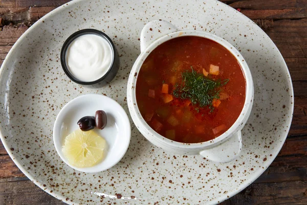 Суп с соленым супом с лимоном, мясом, огурцами, оливками с томатным соусом в миске на пакетике . — стоковое фото